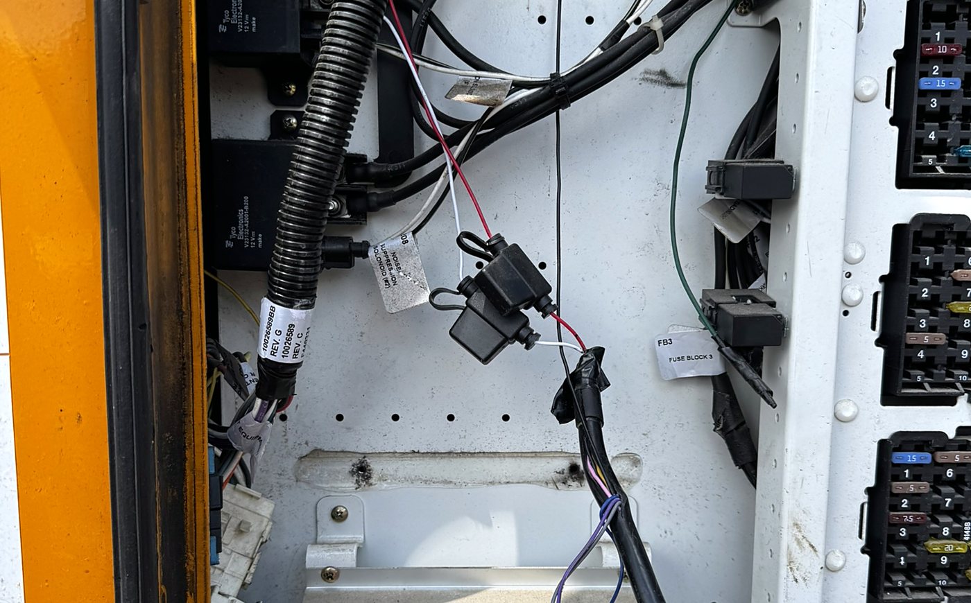 Loose add-on fuse holders and taped splices hanging in a school bus electrical panel