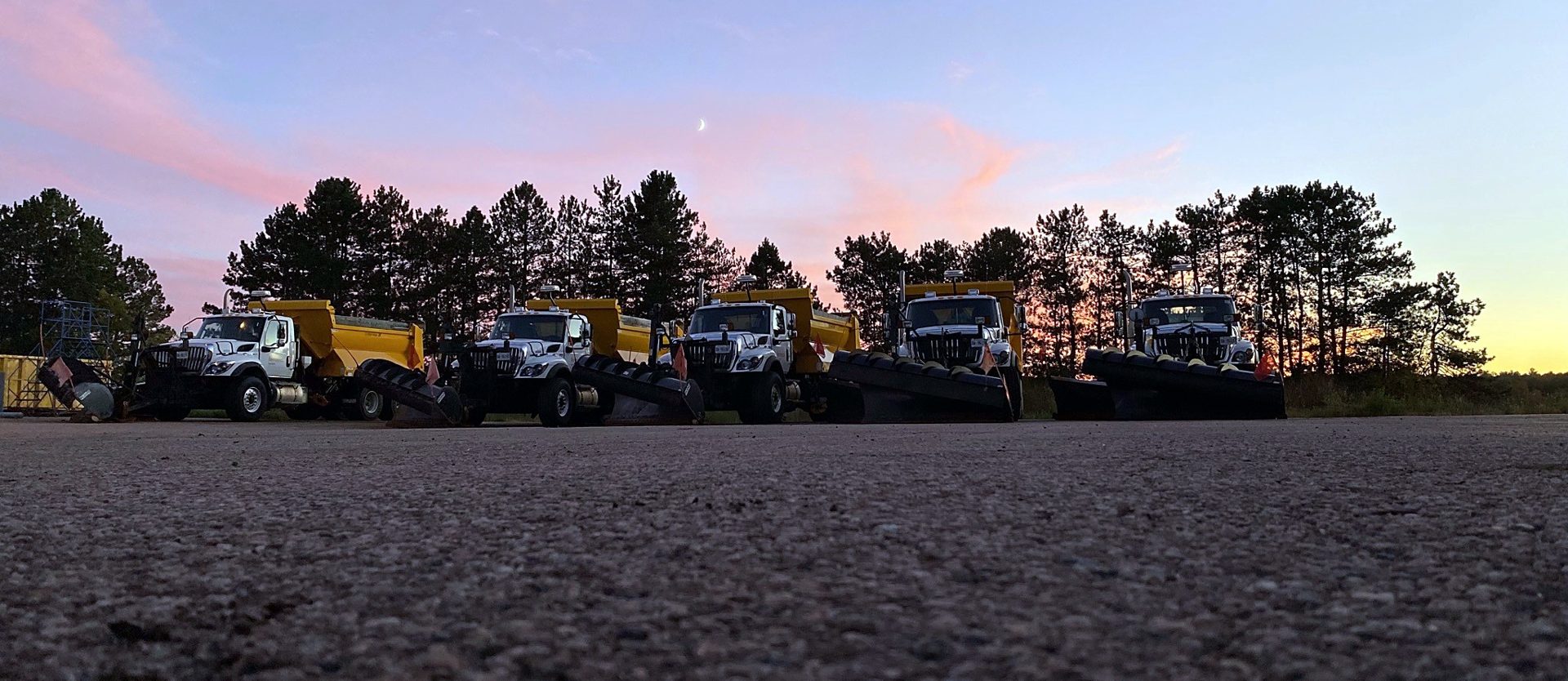 Plow trucks lined up at sunset