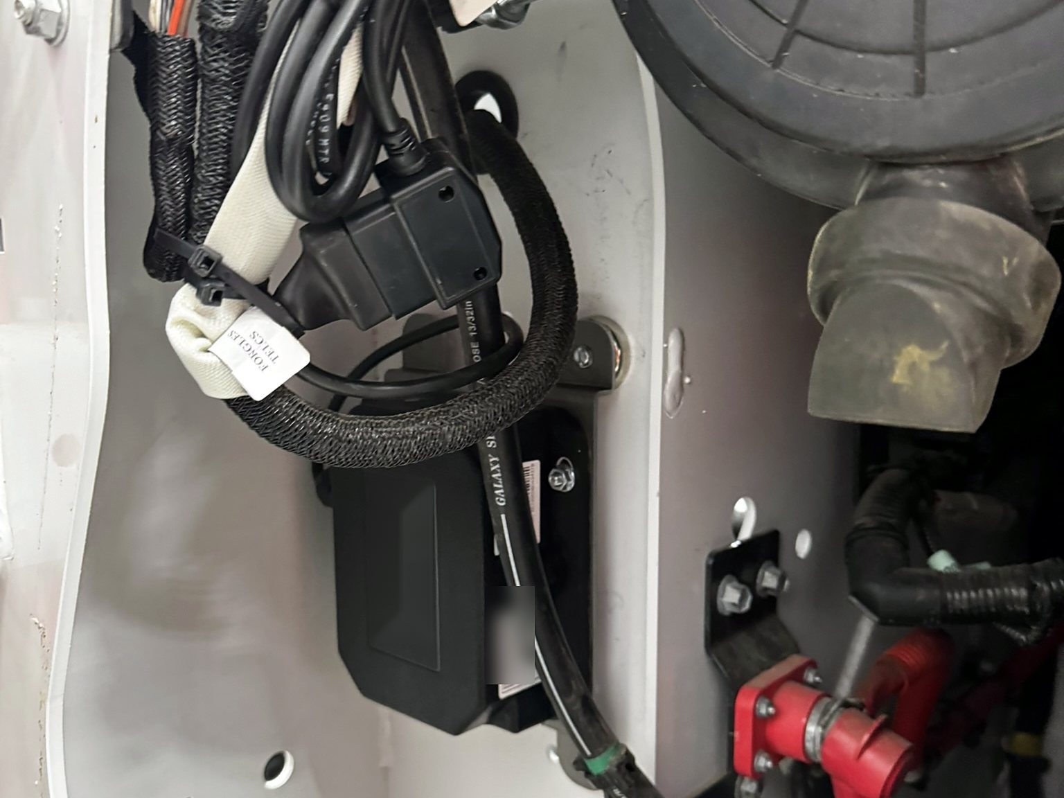 Telematics module bracket-mounted in a bus body panel with the harness sleeved and tied